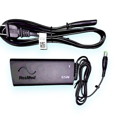 A black ResMed 65W AirSense 11 AC Power Supply with a power cord and surge protector.